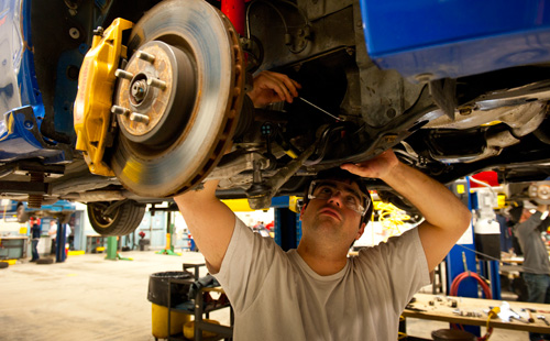 student working under car on lift in automotive lab