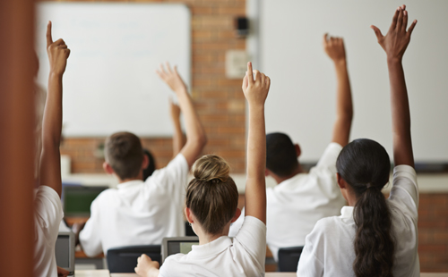 students raising their hands in classroom